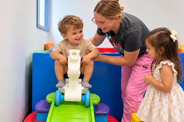Therapist helping a smiling toddler on a ride-on toy